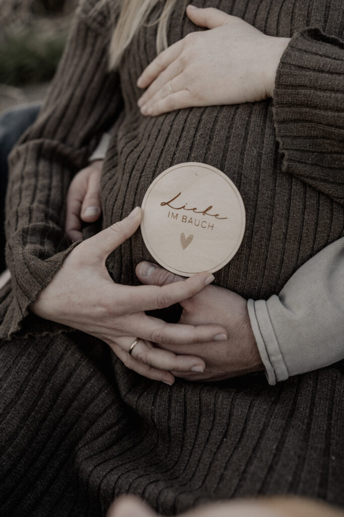 Babybauchshooting. Nahaufnahme Babybauch. Mann und Frau streicheln den Bauch und halten ein Schild "Liebe im Bauch".