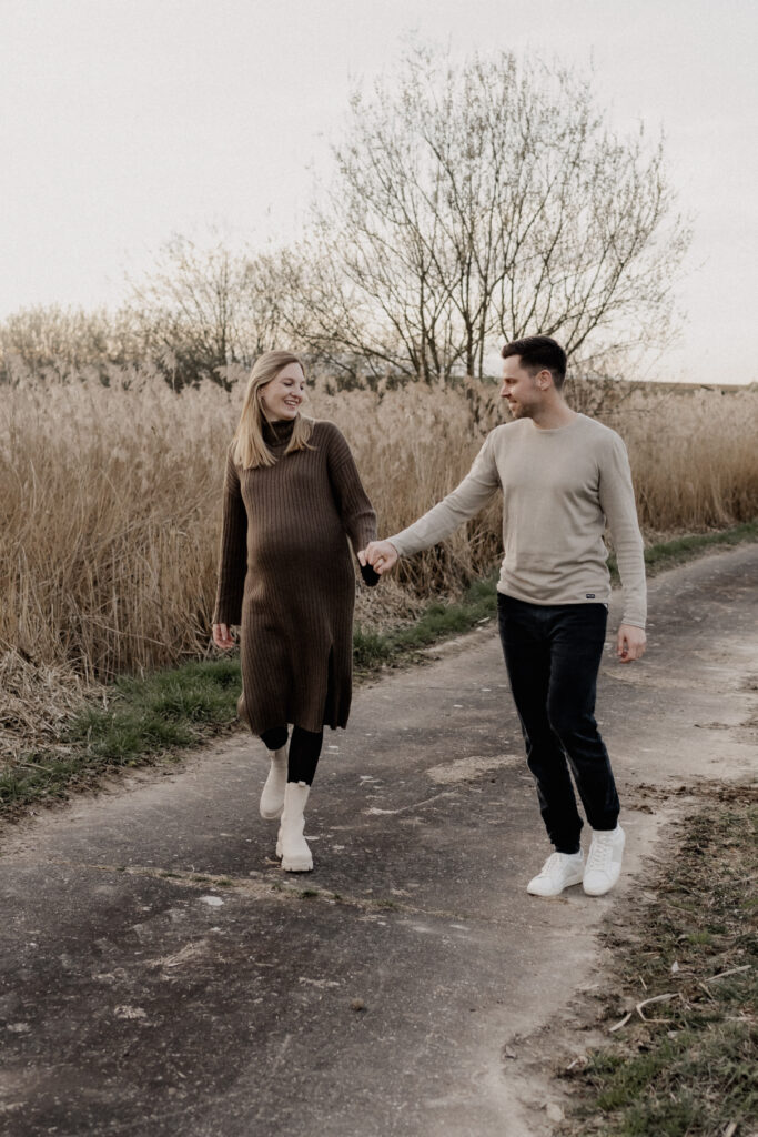 Babybauchshooting mit einem Paar. Beide Laufen Hand in Hand.